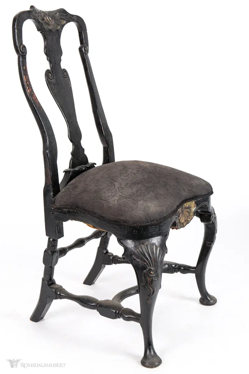 Rocaille på toppstykke og sarg og små volutter på ryggbrett og akterstaver. Skjellformer på stolens knær.
