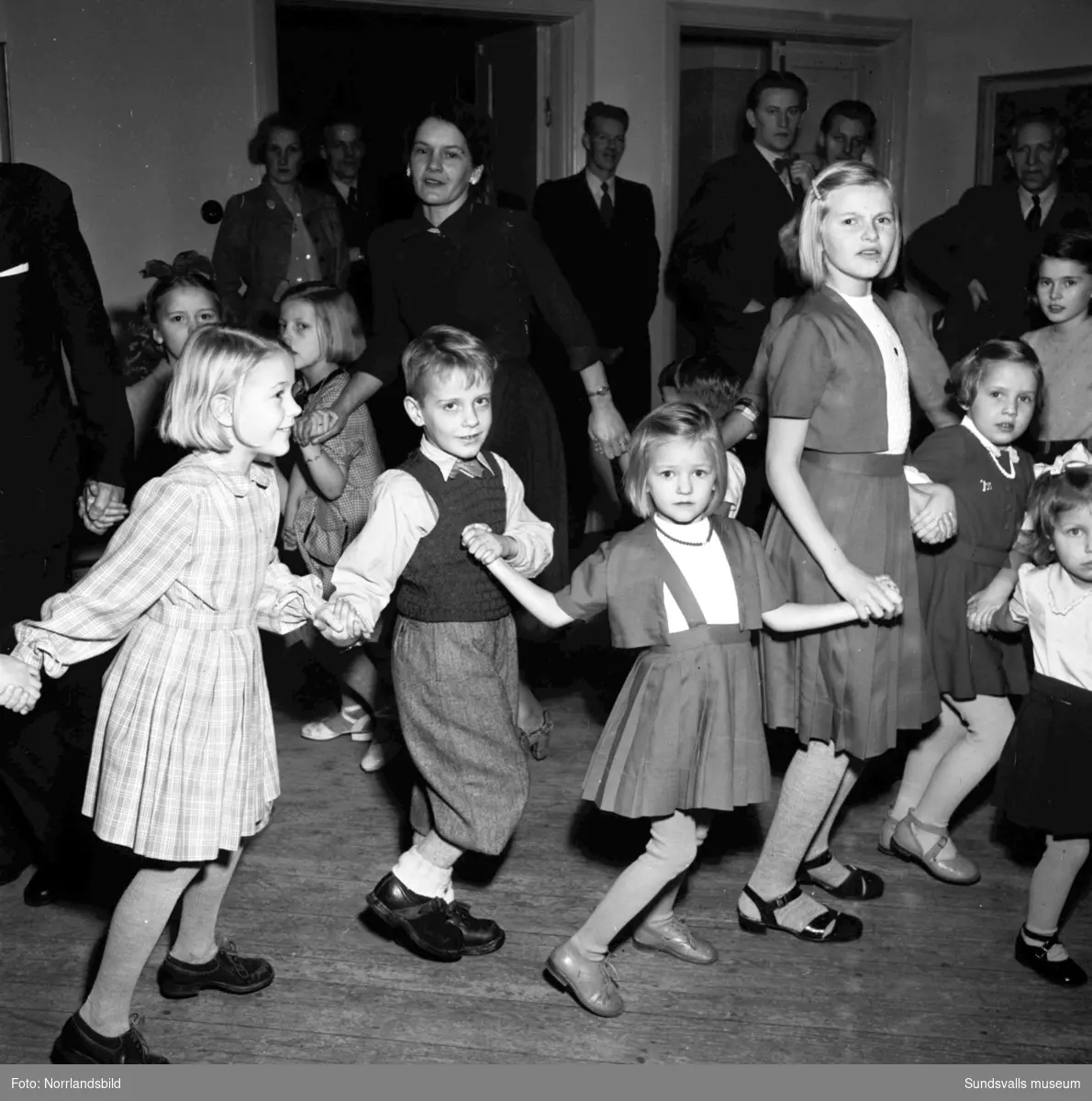 Barnjulfest, julgransplundring, i Sundsvalls Folkets hus. En liten flicka spelar dragspel och långdans med glada barn.