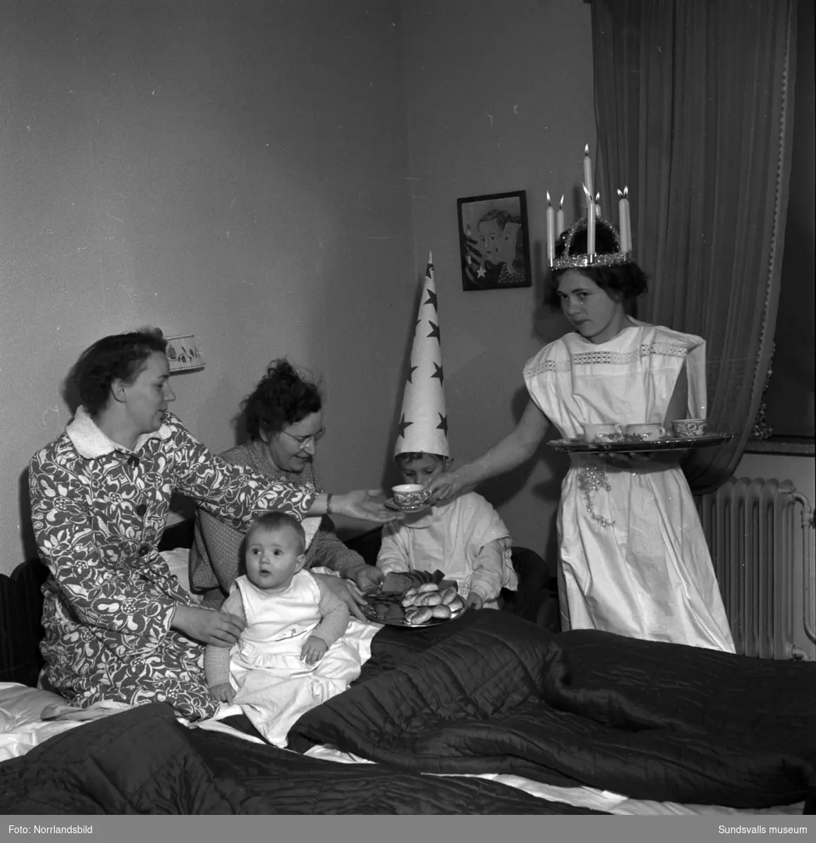 Luciafirande hemma hos familjen Berg. En pojke och en flicka lussar för två kvinnor och ett litet barn.