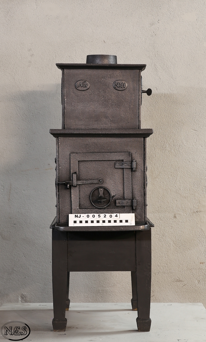 Kokeovn med to muser på enkel profillist. En fløytespillende og en dansende. Begge med draperier. Kokeanretning i topplaten til 1.etg. Ovnsdør på kortside. Rosett på begge sideplatene 2.etg. Den ene er løs og fungerer som ventil. Innskrift på frontplate og bakplate 2.etg. Røykuttak i toppen.