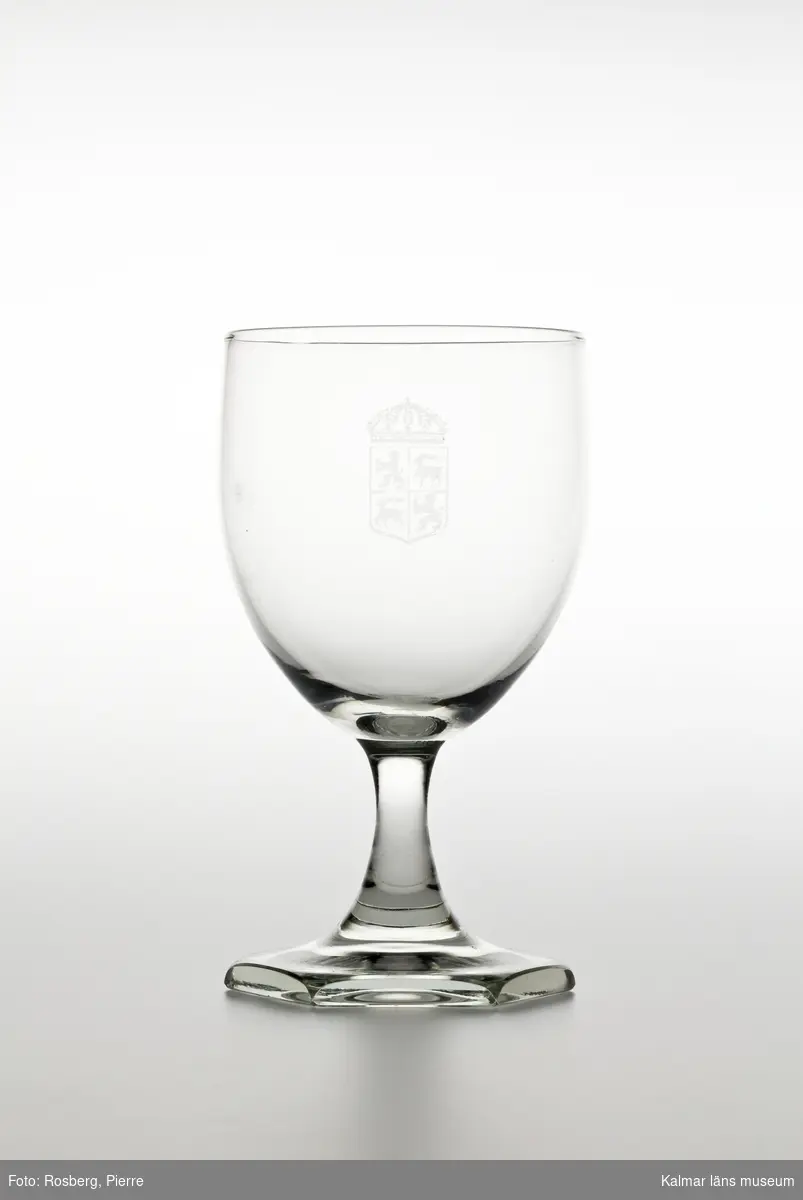 KLM 44717:15 Rödvinsglas, av glas. Glaset är tillverkat av Orrefors glasbruk och kupan är graverad med länsvapnet. Liten flisa saknas på fotens undersida.
