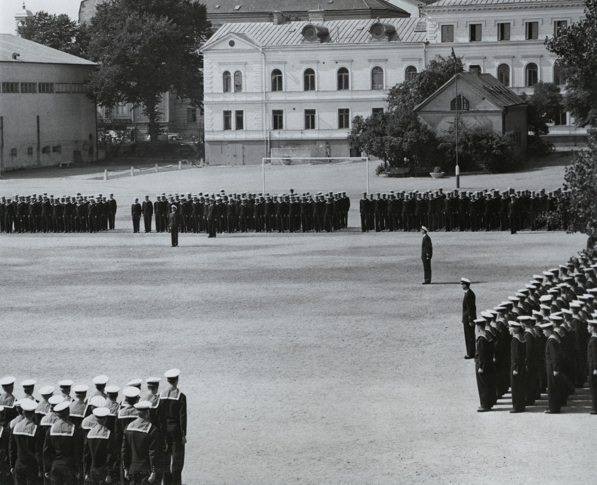Uniformsklädda flottister står uppställda på Sparres kaserngård. I bakgrunden syns bataljon Sparres kanslibyggnad uppförd omkring 1818.