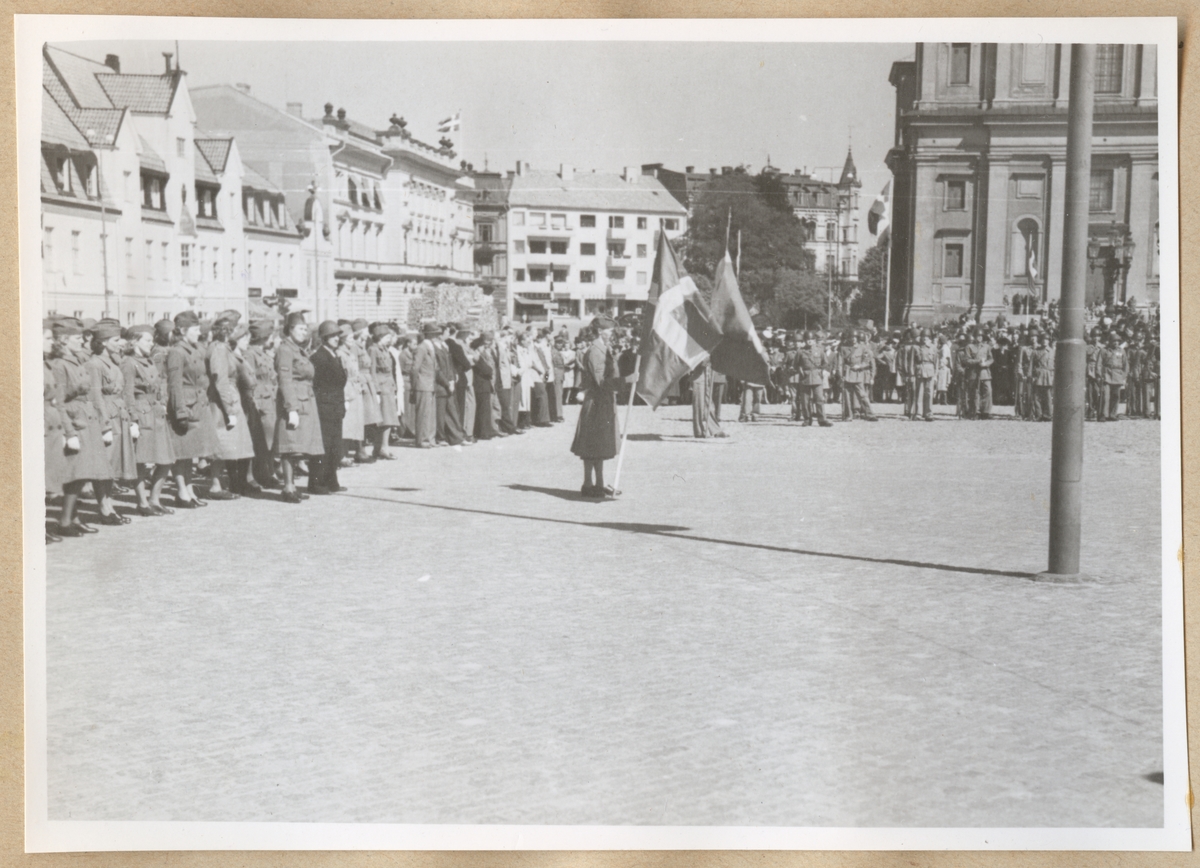 Lottor står uppställda på stortorget, framför Klaipedaplatsen. En av dem står längre fram och håller i en Sverigeflagga. Fredrikskyrkan syns åt höger i bakgrunden och framför den står uppställda soldater.