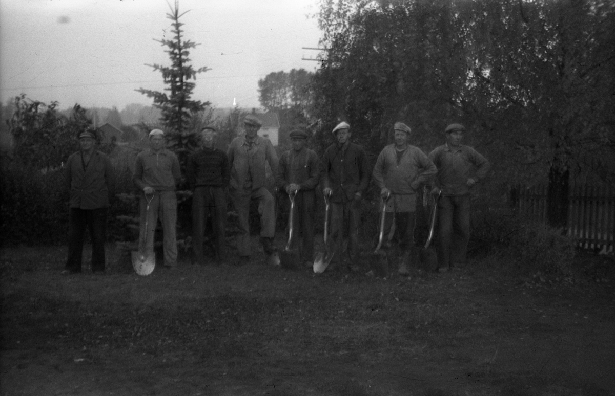 En gjeng grøftegravere fotografert på gårdsplassen på Odberg på Kraby, oktober 1950. Karene gravde grøft for telekabel. Ingen av karene er identifisert.