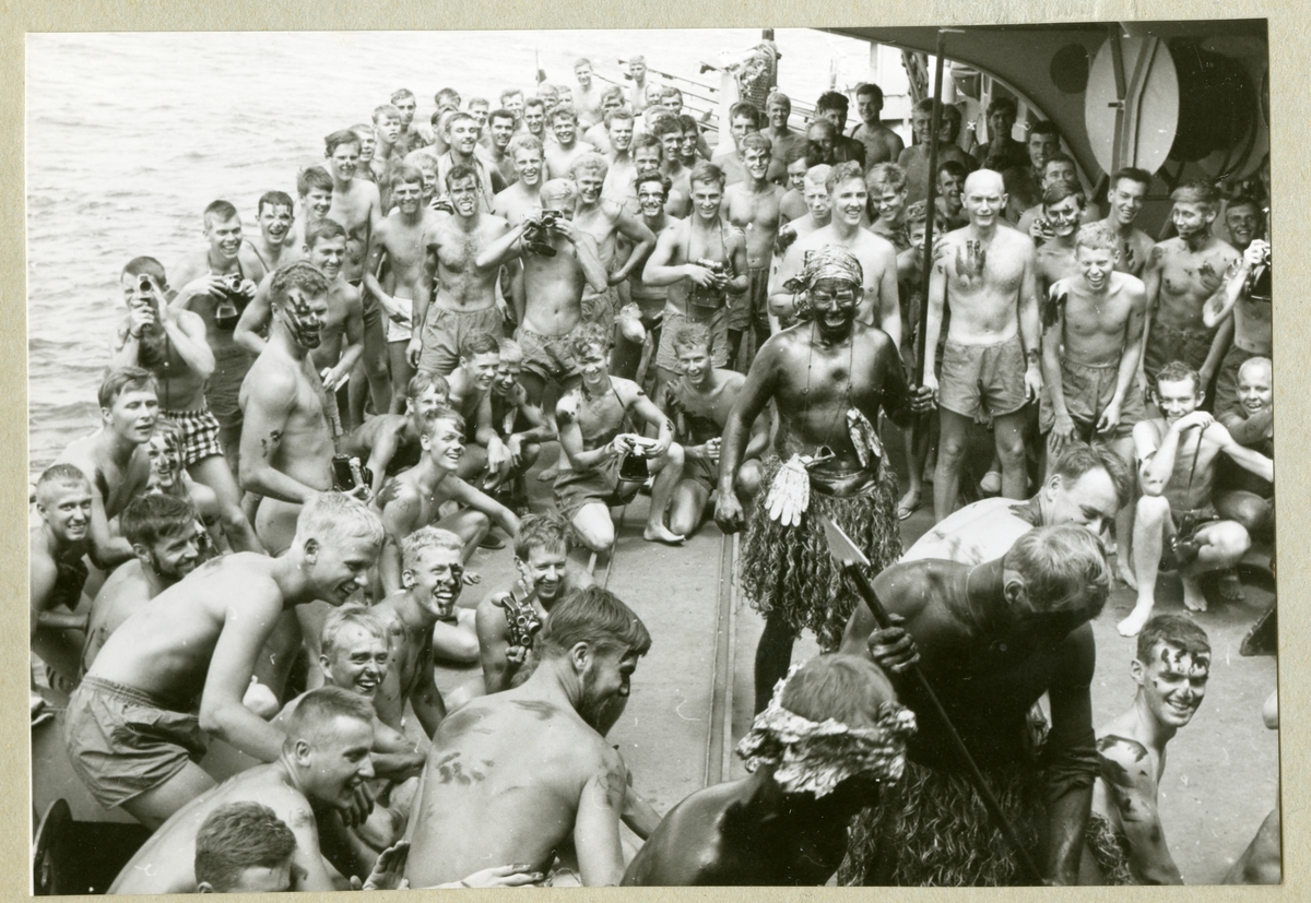 Bilden föreställer bestättningen ombord på minfartyget Älvsnabben som barbröstade står samlade och tittar på ceremonierna kring linjedopet under långresan 1966-1967. En del av männen bär även utklädnad som en del av ceremonin.