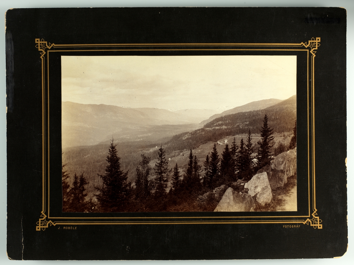 Landskap, mul. Etnedal der fotografen J.E. Robøle fotograferte mye Utsyn over dalføre med skogkledde åser. Gårdsbebyggelse med kornstaur i forgrunnen.