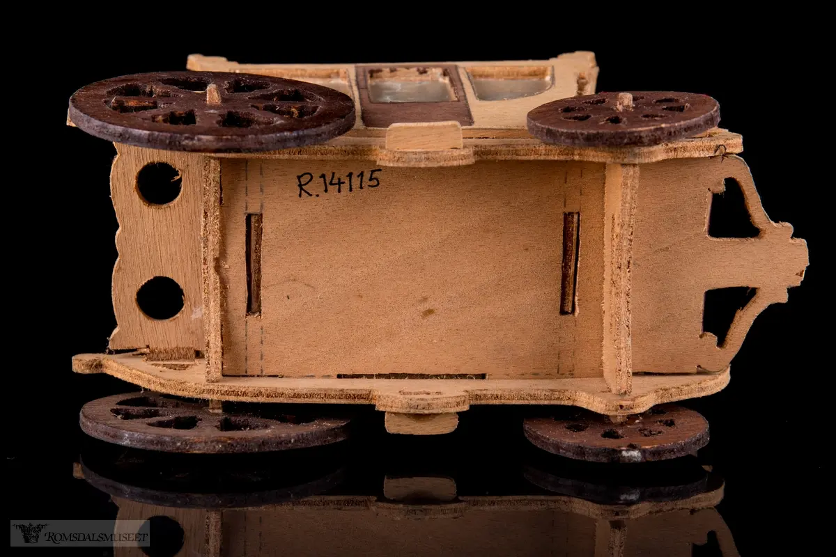 En liten leke- hestevogn i kryssfiner. To store og to små hjul, kledd med rød filt og vokspapir er brukt som vinduer.