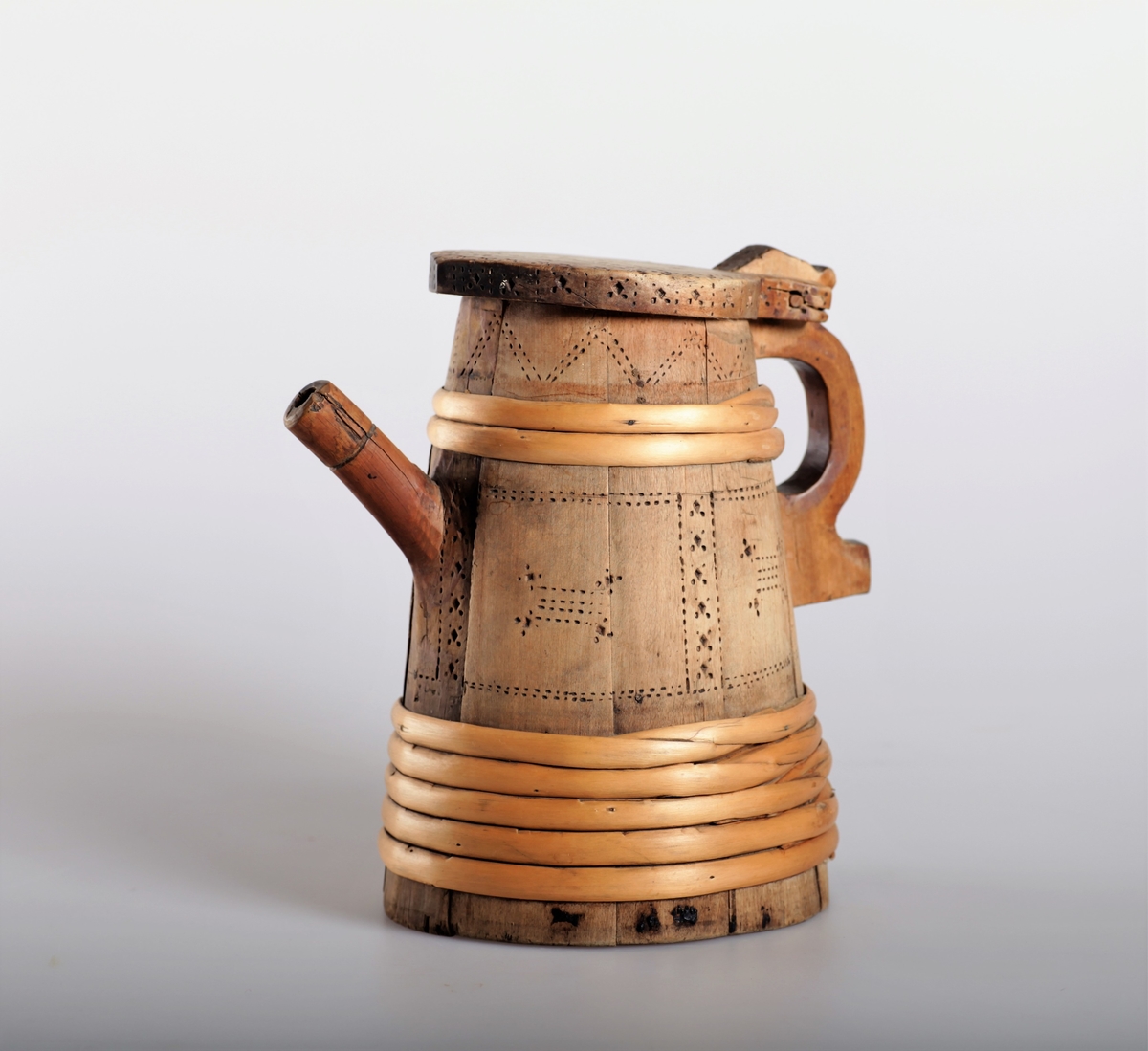 Kanna har tut og er lagget. Trebandene som er sveipet rundt beholderen har en annen patina enn stavene, og der virker derfor som om kannen er reparert i nyere tid. Kannen har innsvidde ornamenter.