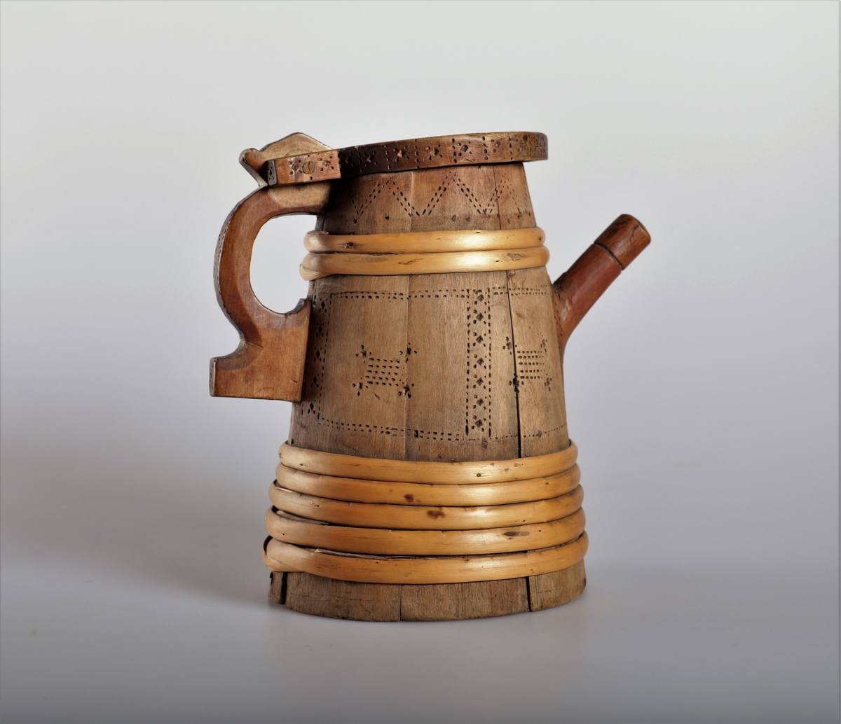 Kanna har tut og er lagget. Trebandene som er sveipet rundt beholderen har en annen patina enn stavene, og der virker derfor som om kannen er reparert i nyere tid. Kannen har innsvidde ornamenter.