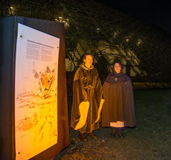 To kvinner i middelalderklær og kapper står foran en svakt opplyst middelalderruin og synger. (Foto/Photo)