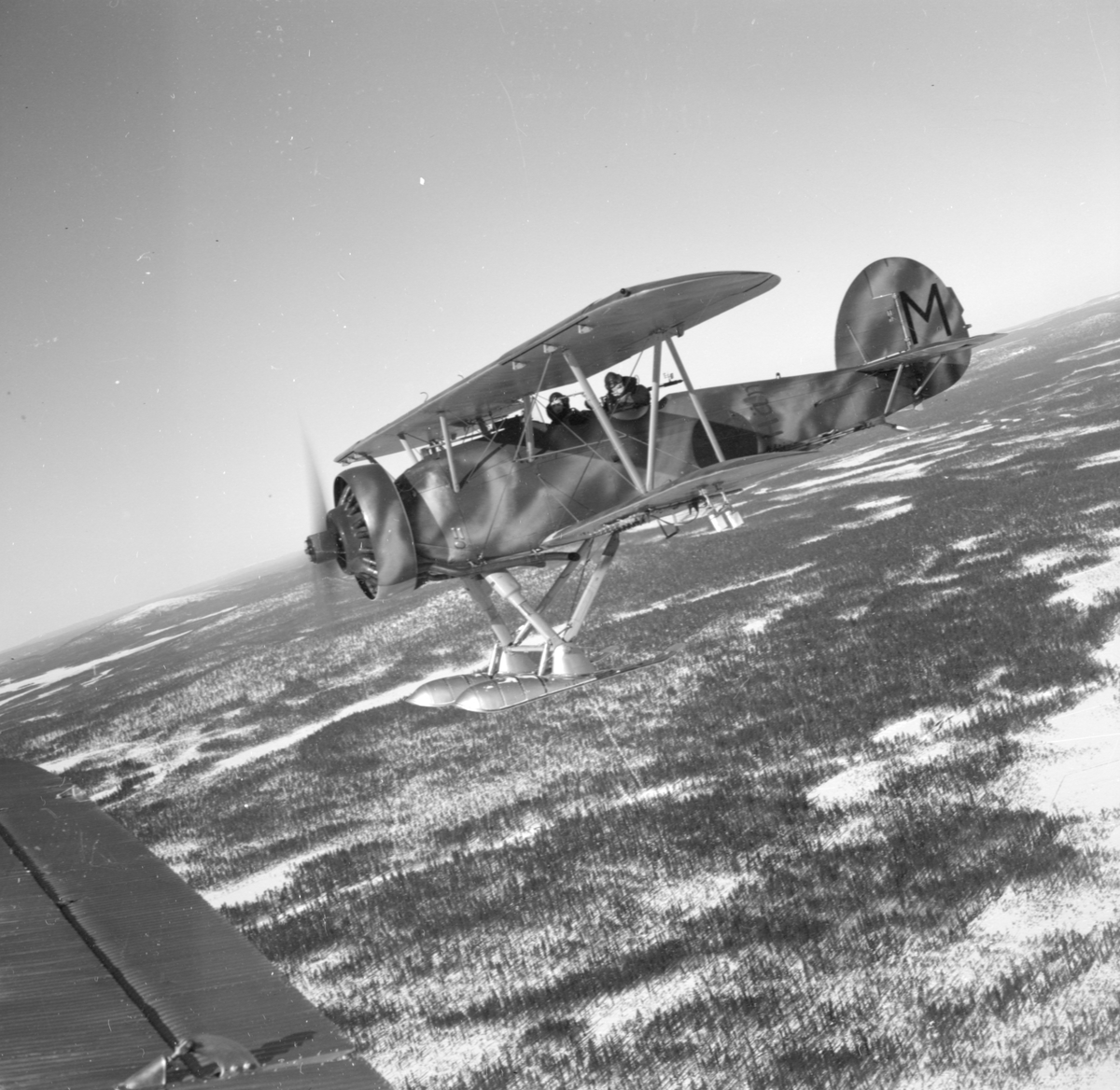 Flygplan Hawker Hart svar M "Hämnaren" vid F 19, Svenska frivilligkåren i Finland i luften över snöigt landskap. Två män i besättningen.