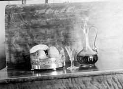 Stilleben, karaffell, glass og fruktfat med frukt.