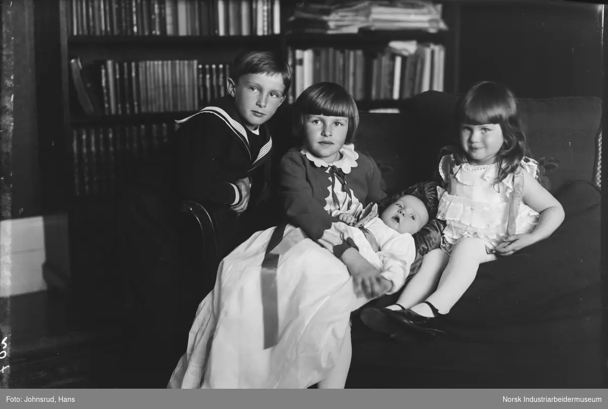 Gruppeportrett av direktør Halvor B. og Willa Holtas fire barn. Bildet er tatt i forbindelse med dåpen til Øyvind Holta. Barna sitter i en sofa med dåpsbarnet kledd i dåpskjole i fanget på eldre søster Anne Marie.