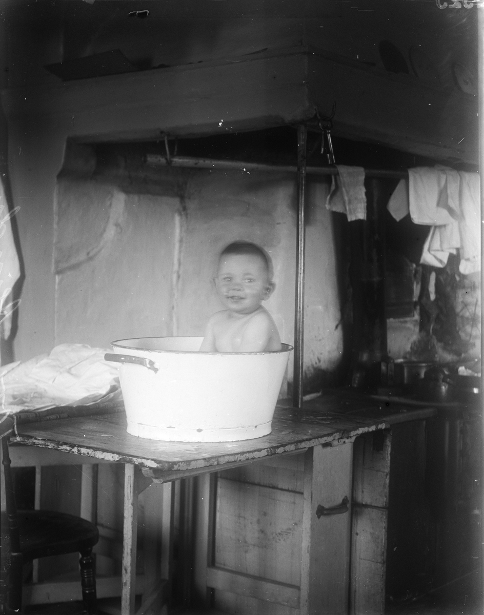 Tore Alinder badar i balja på bord i köket, Sävasta, Altuna socken, Uppland 1925