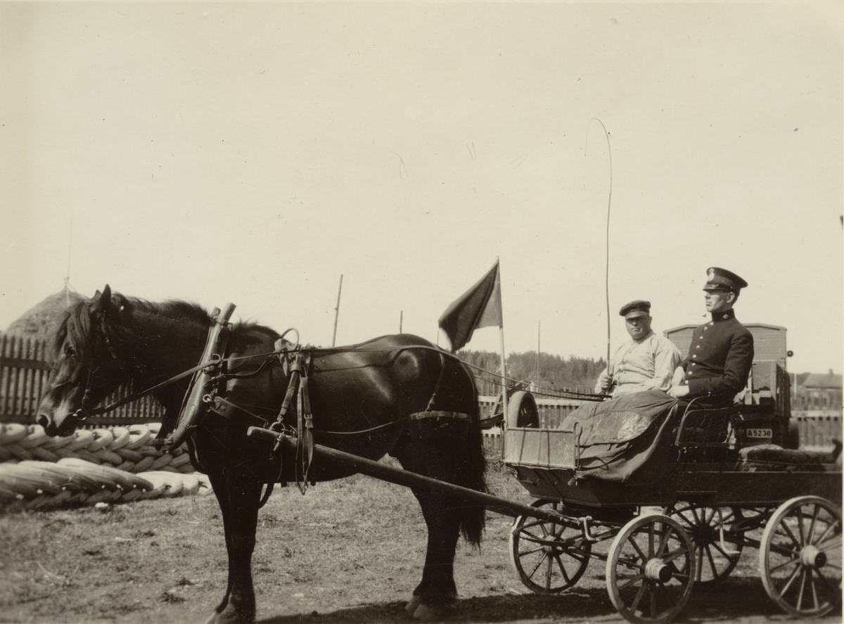 Två män på vagn dragen av häst.
Finnvikskabeln. Dynamittransport. Ur albumet Kabelarbetet Hjälmsälra (Hjälmsättra) - Norrtälje -  Finnviken utfört under sommaren 1928.