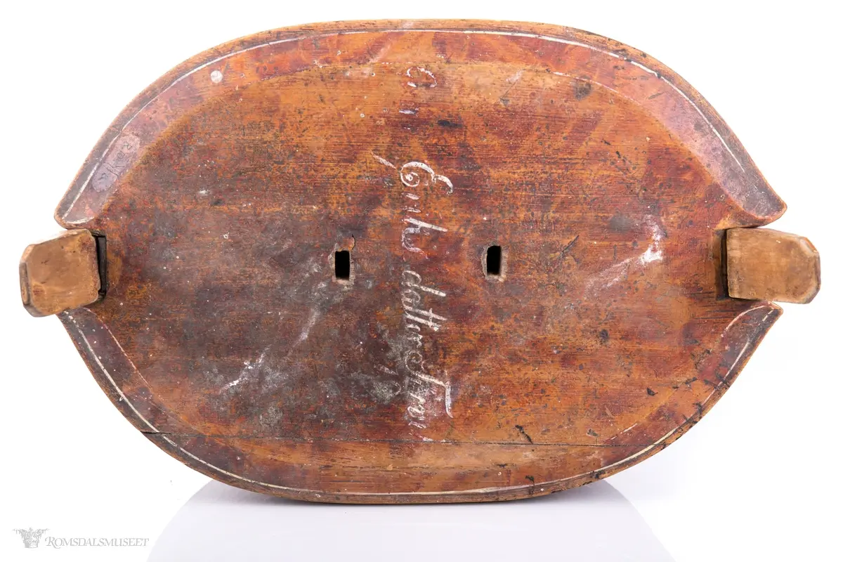 Hvite linjer langs kanten. Avrundet lokk. Innskrift.