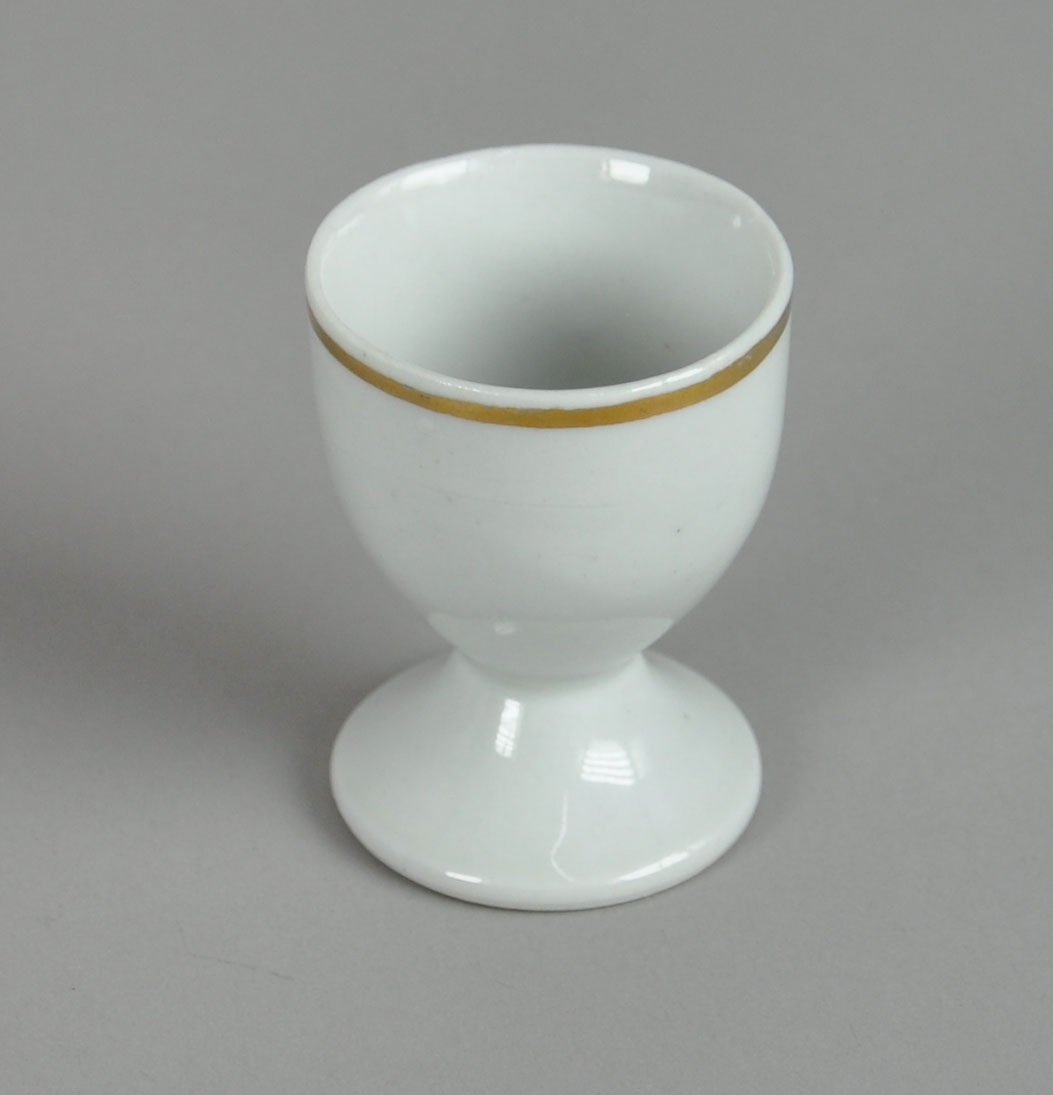 Eggeglass av glassert keramikk, med stett. Ved munningsranden er det en påmalt stripe i gullfarge.