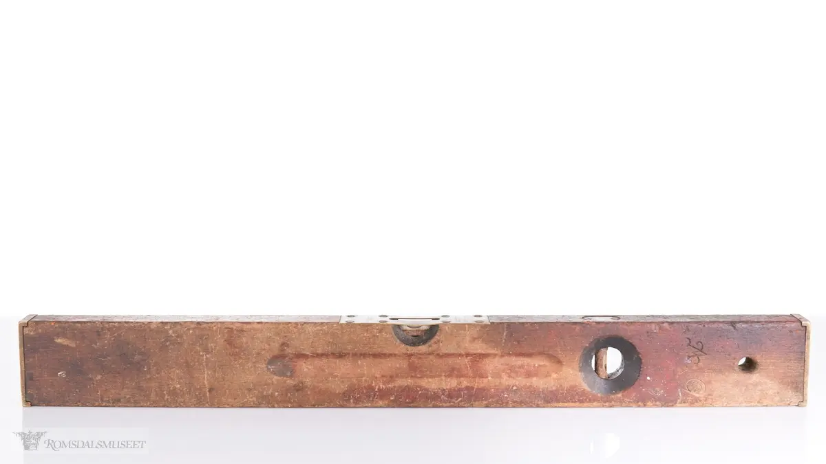 Rektangulær trevater med topp- og endeplater i messing og to bobler. Ovalt utfreset spor på begge sider av vateren. Gjennomgående opphengshull.