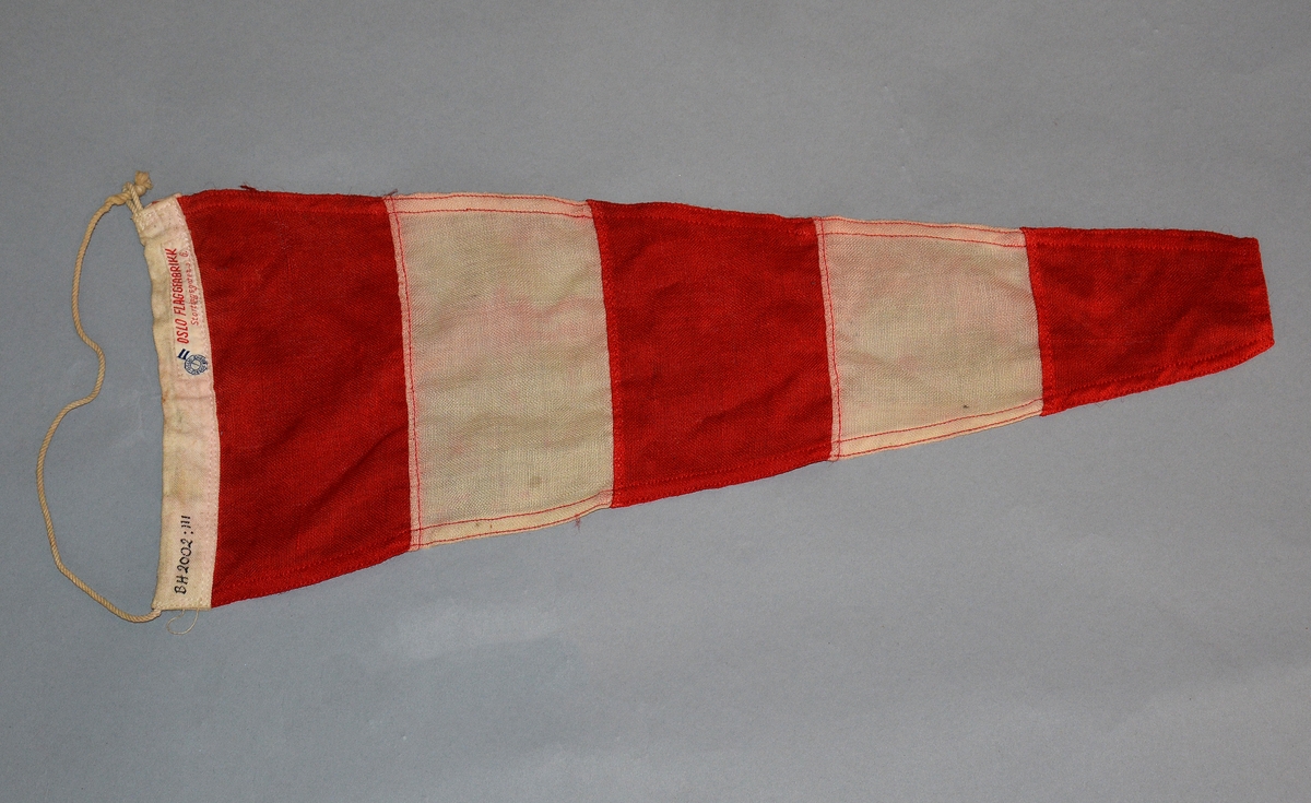 Trekantet flagg med røde og hvite striper, består av fem trapesformede stykker som er sydd sammen. Påsydd tvinnet snor til å feste stenderen med. Brukes til å markere at seilregattaen er utsatt inntil videre.