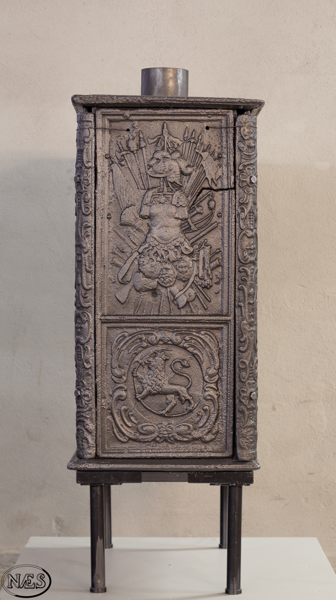 Kasseovn med ovnsdør på kortsiden og røykuttak i topplaten. Ovnen har løse skinner med bruskornamenter. På langsidene er Gyldenløves våpen omgitt av krigerske emblemer med innskrift i knekket bånd over. Øverst står det innskrevet ANNO og nederst på platen 1687. På kortsiden er det øverst krigerske emblemer og nederst den norske løve omkranset av brusk-kartusj.