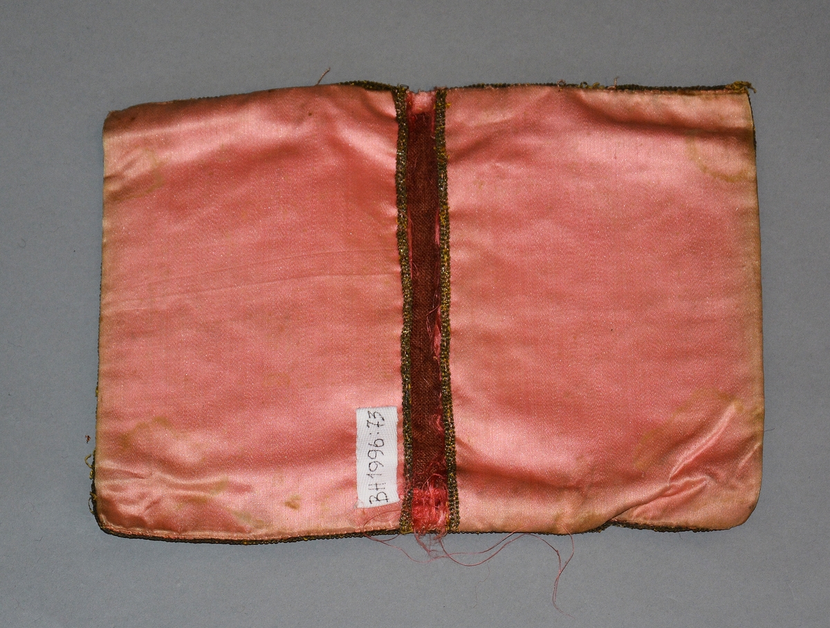 Lommebok i håndsydd rosa silke, kantet med gullbånd. Pyntet med paljettbroderi på utsiden. Bordert "MM 1787" på forsiden og "Fra en ven" på baksiden. Rektangulært formet med lomme på begge sider, kantet med gullbånd. Fôret med brun lin.