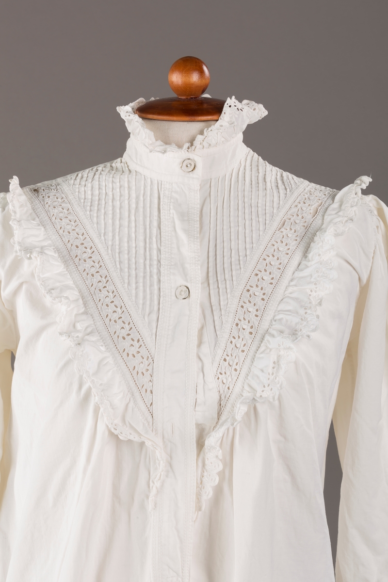 Form: Lange ermer, fotsid.

Blondekant og rysjer i halsåpning.
To knapper i metall kledd i tekstil. Mangler en knapp.