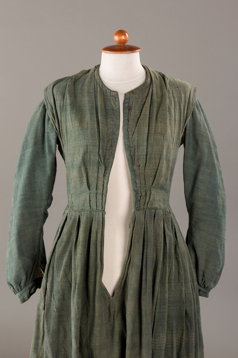 Form: Trangt liv med legg foran, skjørtet sydd med legg i livet.  God vidde i skjørtet, lange armer. Fem hekter i livet mangler.