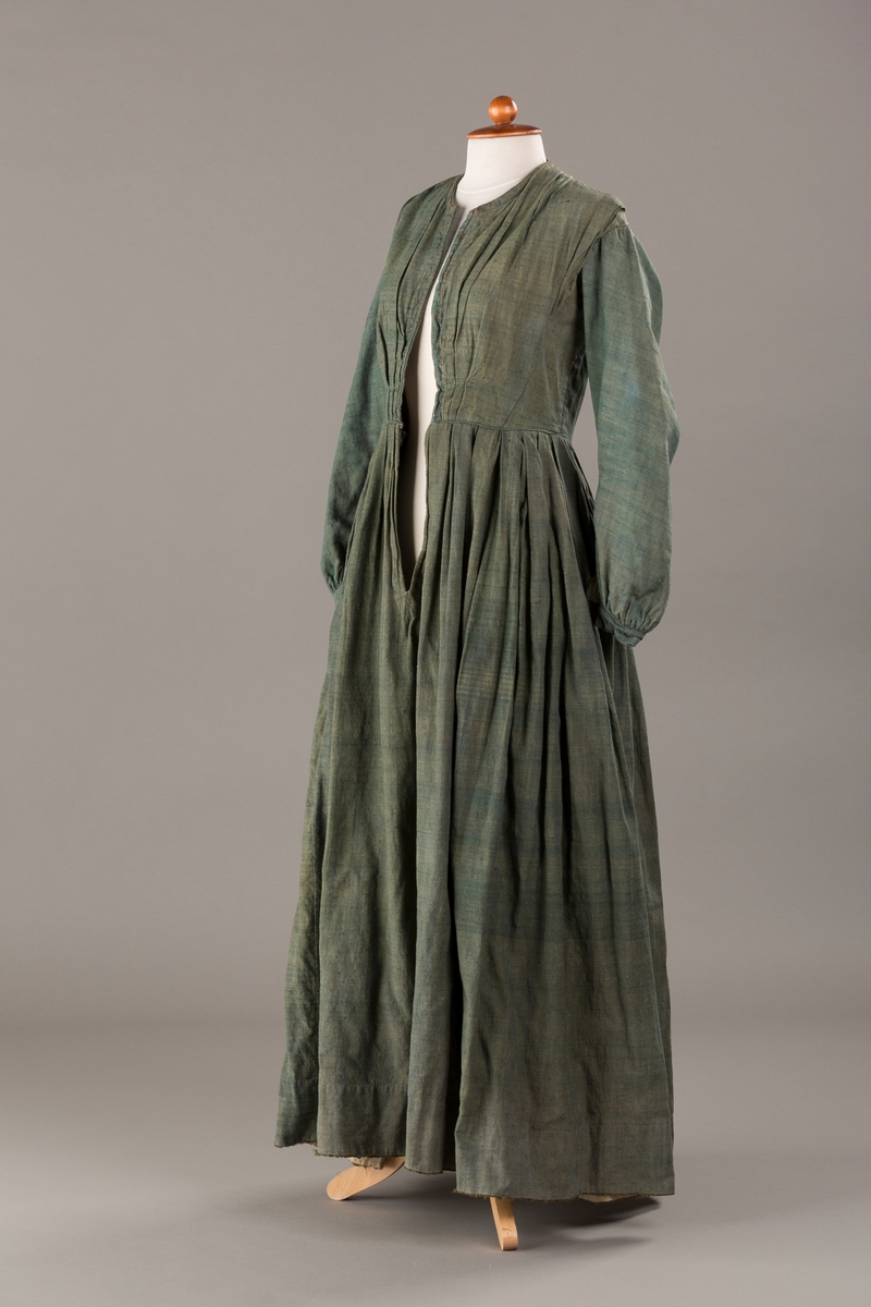 Form: Trangt liv med legg foran, skjørtet sydd med legg i livet.  God vidde i skjørtet, lange armer. Fem hekter i livet mangler.