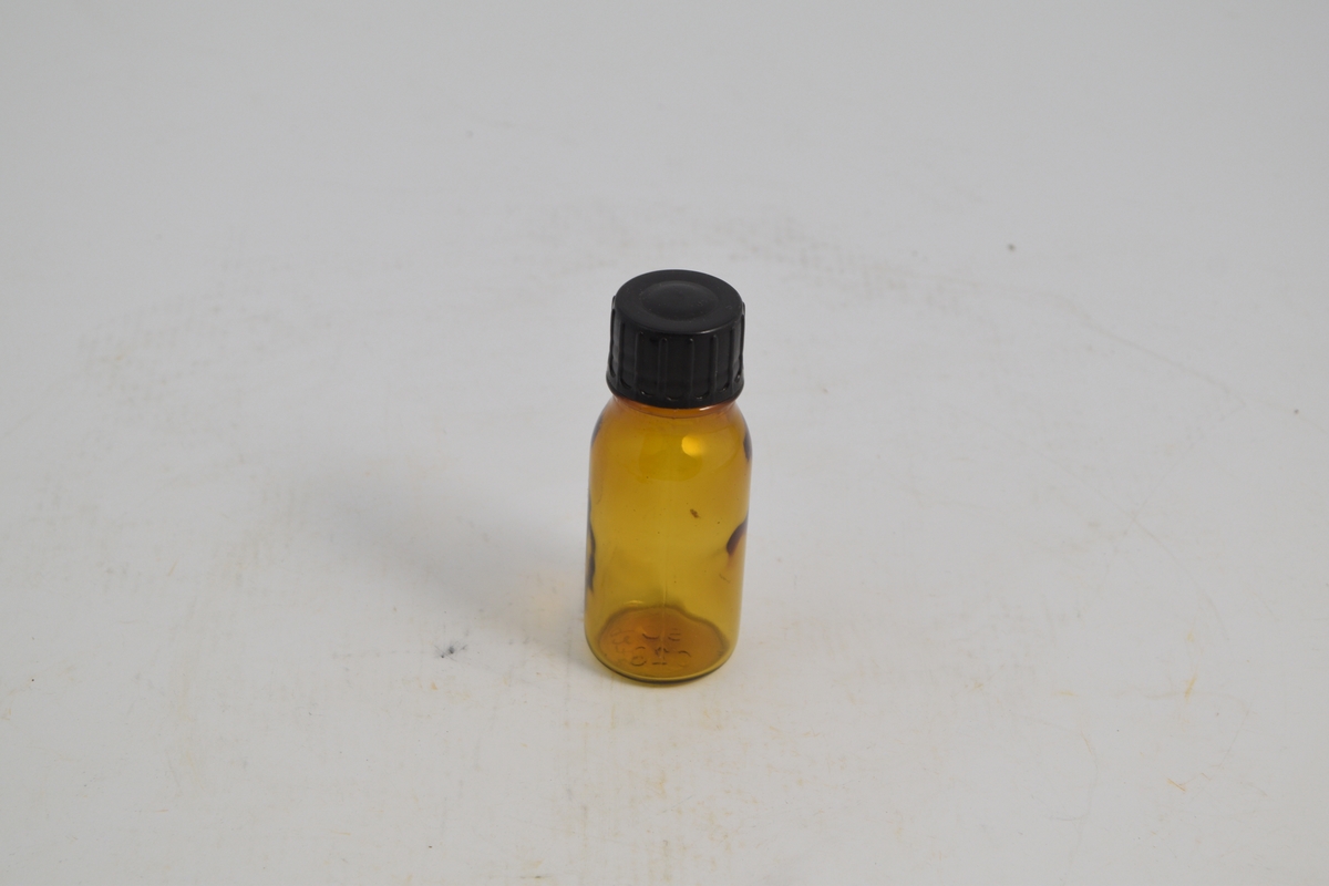 Brun transparent rund flaske med smal hals og plastkork, skru. Ble brukt til salg av flytende legemidler fra 1960 og fremover.