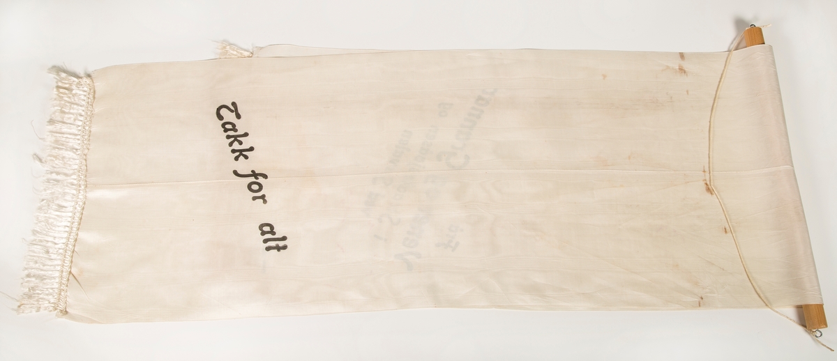 Stort sørgebånd til begravelse. Festet til rundstokk for oppheng på vegg. Til Garborgs begravelse.