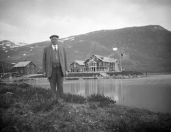 Mann står ute med stort hotellbygg som ligger ved vann i bak