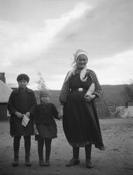 To små jenter og en kvinne med hvitt skaut, rutet skjorte og