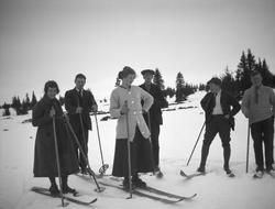 En gruppe på to kvinner i skjørt og 4 menn er ute på skitur.