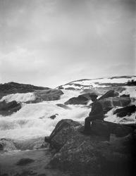 Mann sitter ved elvestryk på fjellet.