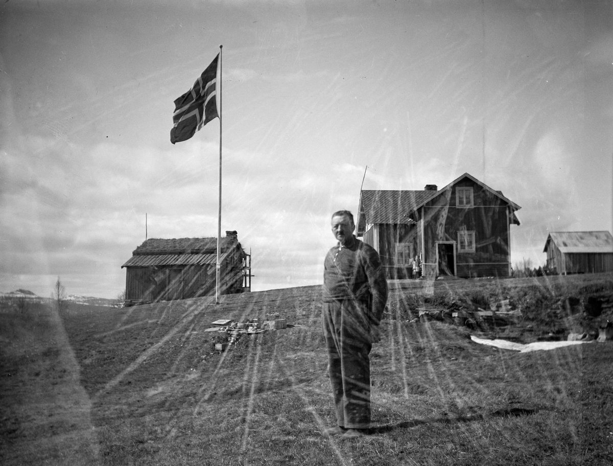 Mann ved hus,uthus og heist flagg på fjellet.