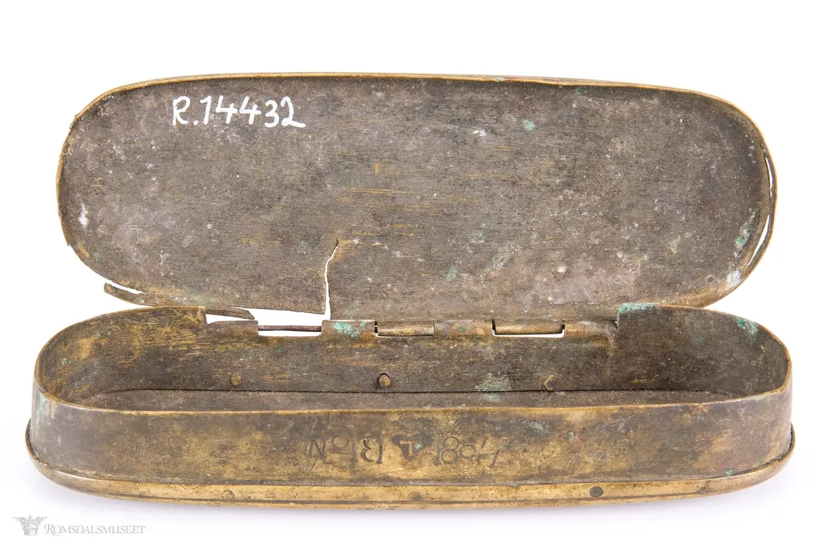 Rektangulær messingeske med avrundede ender. Har en påsatt og påklinket utenpåliggende bunn og utenpåliggende, hengslet lokk