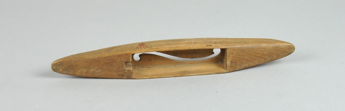 Avlang vevskyttel av tre med uthuling på midten, der hullet i bunnen er formet som en ranke.