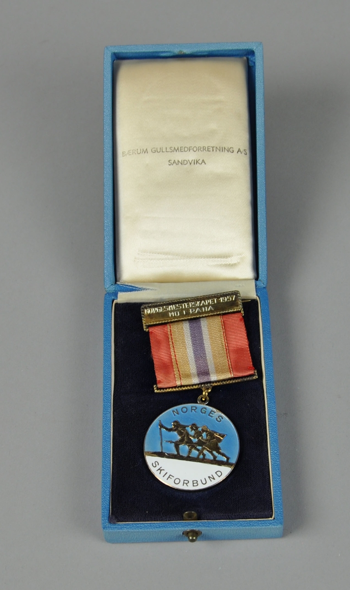 Medalje i etui. Medaljen viser tre skiløpere (Arnljot Gelline, Torodd Snorreson og følgesvenn), på blå og hvit bakgrunn. Bånd i rødt, hvitt og blått.