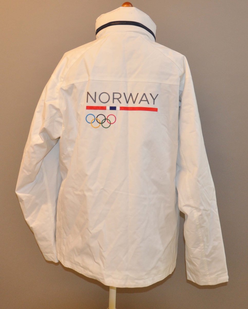 Hvit vinterjakke med glidelås og store lommer. Deltagermerke på venstre bryst og de olympiske ringer på ryggen. Mørkeblå glidelås i halsen for hette. Mørkeblått fleecefor med norsk flagg i ryggen.