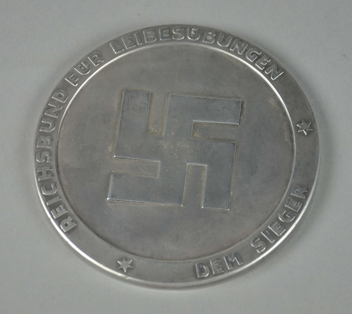 Rund sølvmedalje med byvåpenet for Garmisch-Partenkirchen i midten og tekst rundt kanten. På baksiden hakekors med tekst rundt kanten.