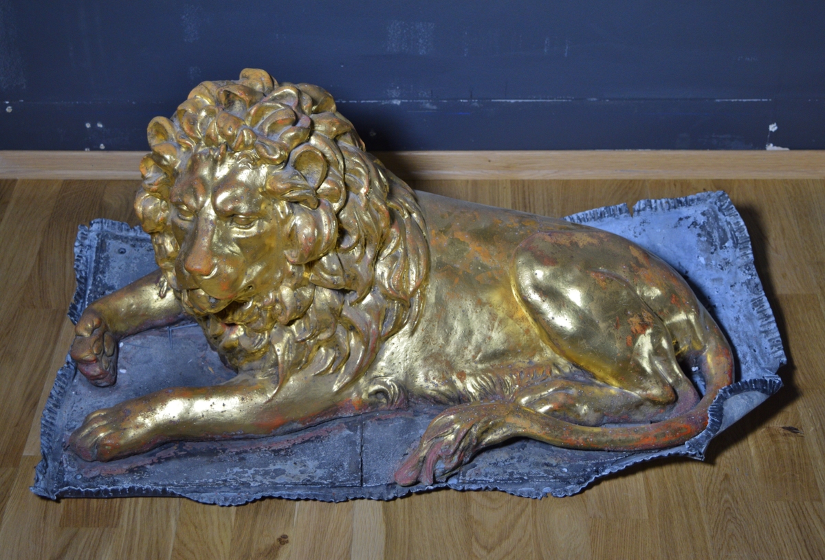Løve-figur dekket med bladgull, liggende på en plate.