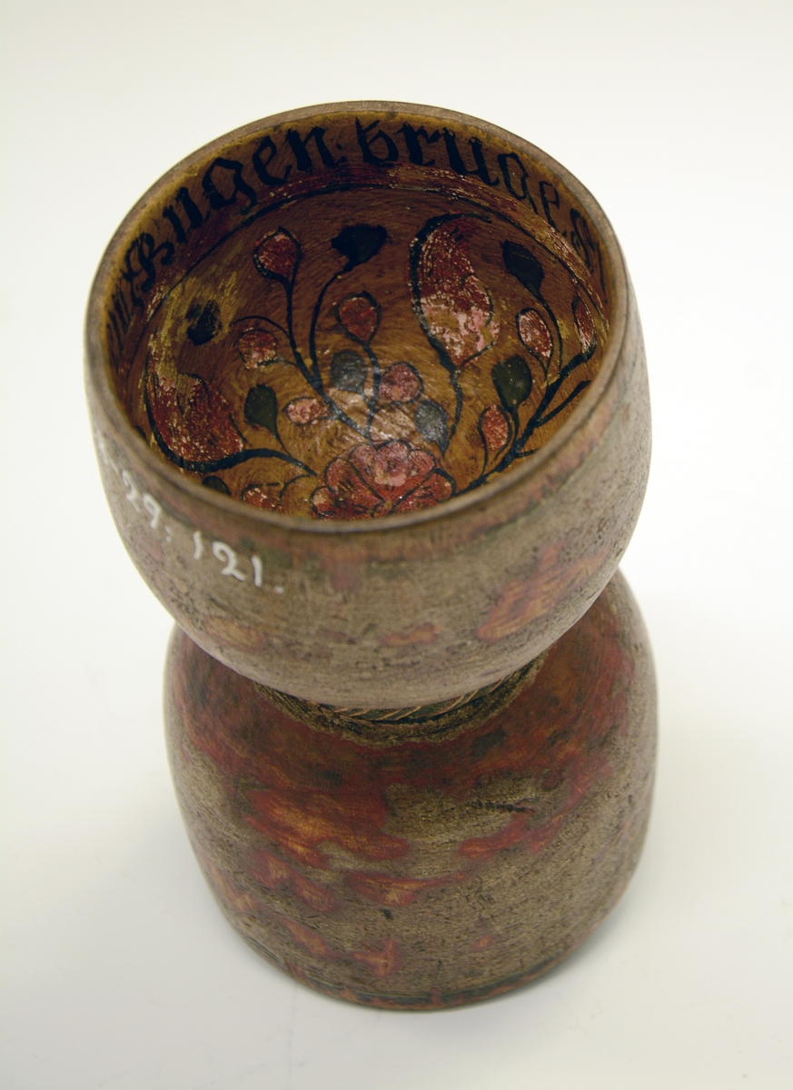 Dobbeltbeger. Fra protokollen: Bugge svarva av bjørk, maala. Baae staupi av paa lag same storleik, innsnørde med eit toglaga band. Utanpaa er den graa-raude maalingi noko avsliti, inni er rosemaala paa gul grunn med raude og grøne rosur, svart konturer. I det eine staupet er ein liten raud botnblom, og fraa denne gjeng mjuke rislur med tytebærblad paa. Kring tromi inni denne innskrift: "Bugen bruges i Fleng af Pige og Dreng". I det hitt staupet er maala eit stort firblad danna av 4 tulipanlaga blomar ut fraa ein botnblom. Millom tulipanane tytebærblad. Innskrift kring tromi inni "O.A.S.M. ANNO 1766"