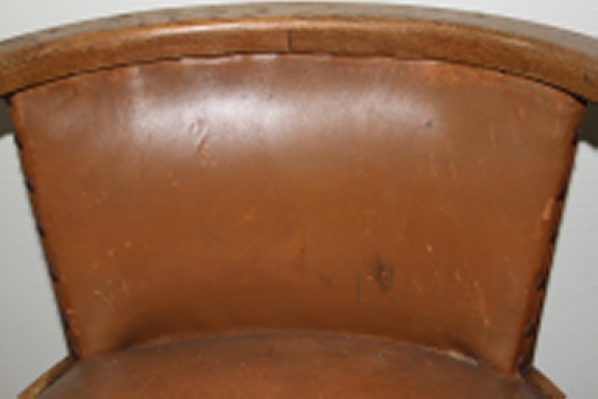 Møteromstol/kontorstol med armlener samt buet rygg. 4 ben. Metallbeslag under armlener. Brunt skinn i rygg og sete. Stolen er lakket med klar lakk. Originalt møbel innkjøpt til det nye Statsarkivet i Kristiansand i 1935.