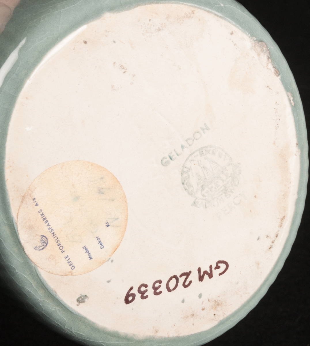 Tillbringare av flintgods, modell -BA, formgiven av Arthur Percy för Gefle Porslinsfabrik. Smal, uppåtsträvande profil med lodgrepe. Aningen oval i formen. Buken vertikalt räfflad. Hög, uppåtböjd och spetsig snip. Glasyr "Celadon 2", ingående i den ugnsfasta serien "Corona" tillverkad 1955. Färgen grågrön, insidan gräddgul. Grön skorstensstämpel på vit grund med text "Celadon Upsala-Ekeby Gefle Made in Sweden Percy". Vidare är "Gefle eldfast" stämplat i massan.