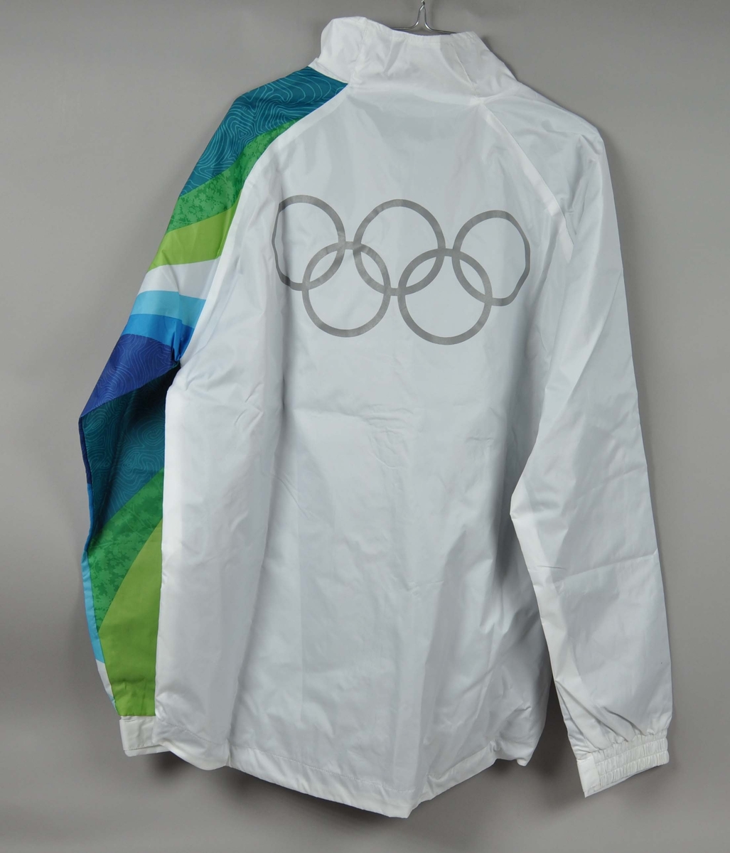 Hvit jakke med flerfarget erme. Motiv av de olympiske ringene laminert på ryggen. Logo for fakkelstafetten i forbindelse med de olympiske vinterleker i Vancouver 2010 er laminert på brystet.