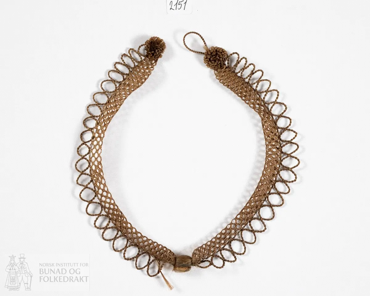 Smykke laget av menneskehår. En nettingformet klave kantet med løkker. Lukkes bak med en knapp og hempe som også er av hår.