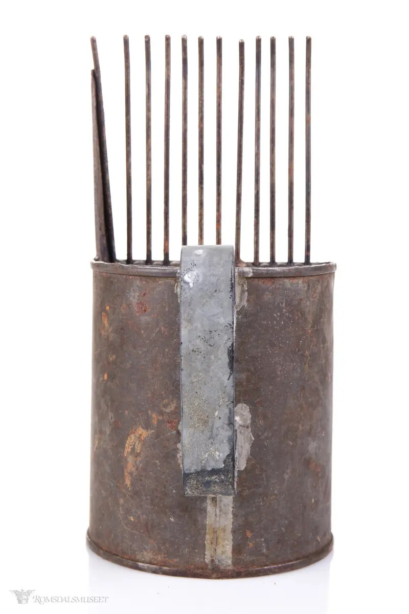 Sylinderformet blikkboks som kropp, med påloddet buehåndtak og en skråstilt plate med tenner foran.