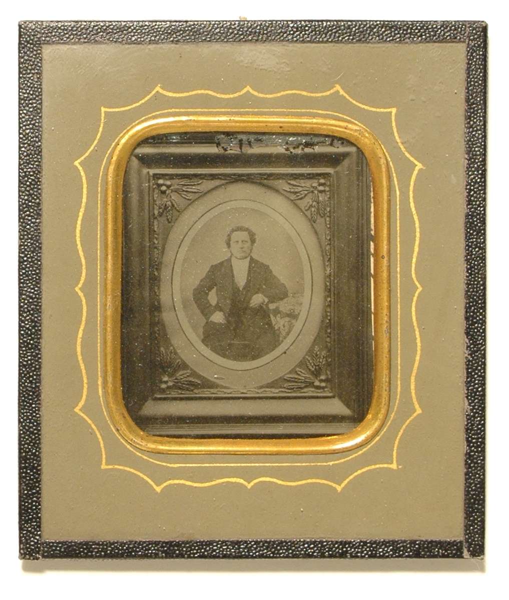 Ambrotyp monterad med klotkant bakom glas; förgylld kant runt fotografiet och guldlinje på kartongen.

Föreställer ett inramat fotografi av en okänd man.