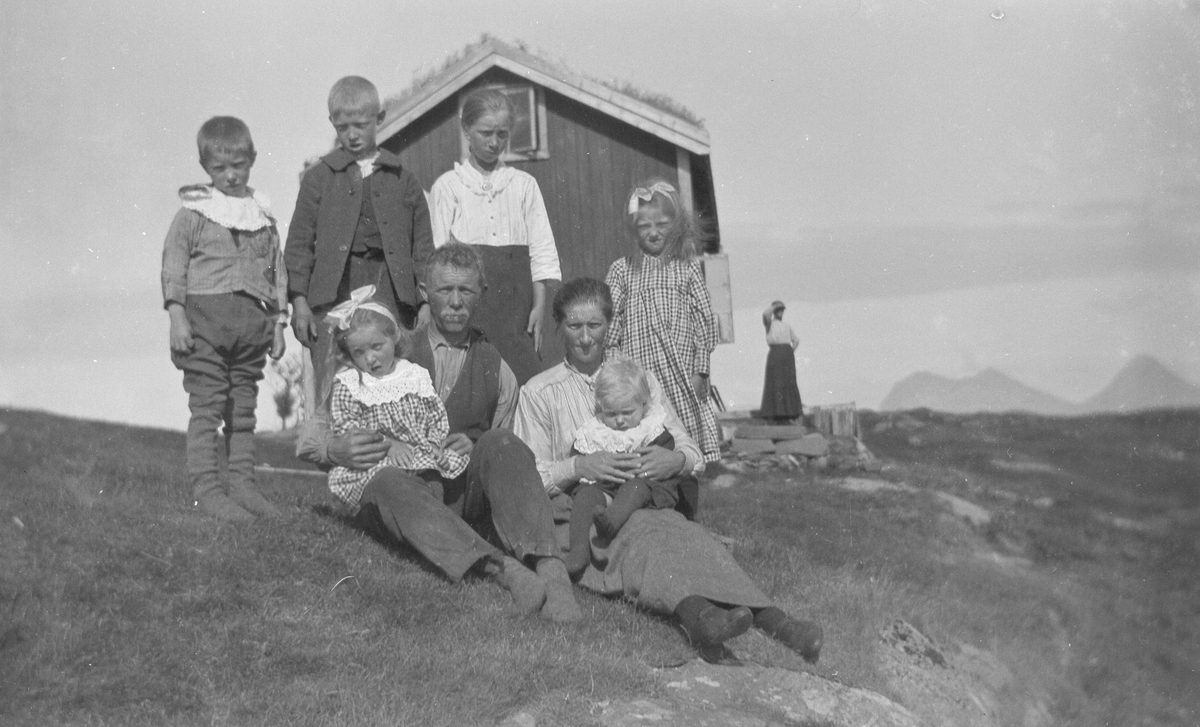 Kvinne og mann med to gutter og fire jenter foran hus.