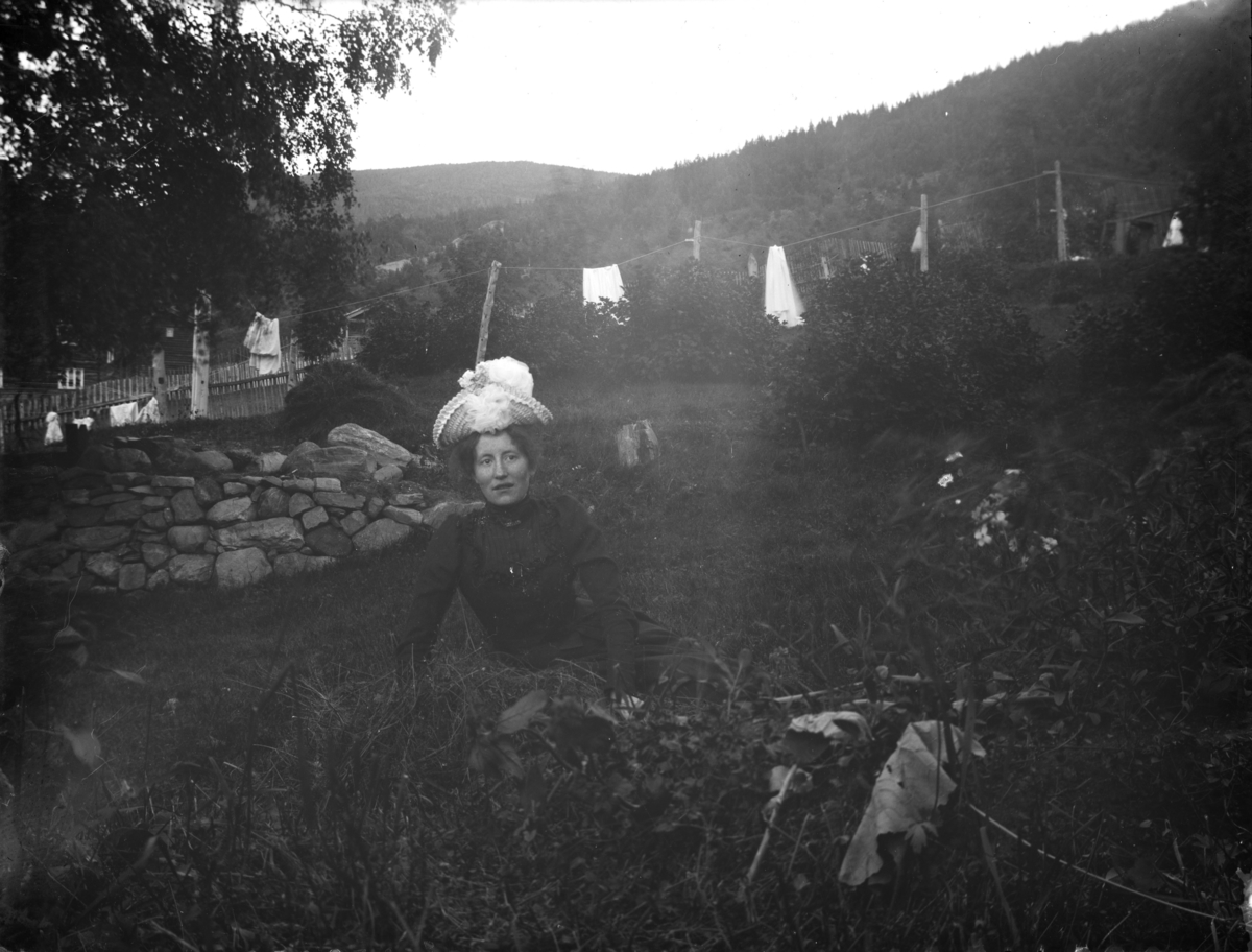 Kvinne med hatt sitter i gresset i hagen